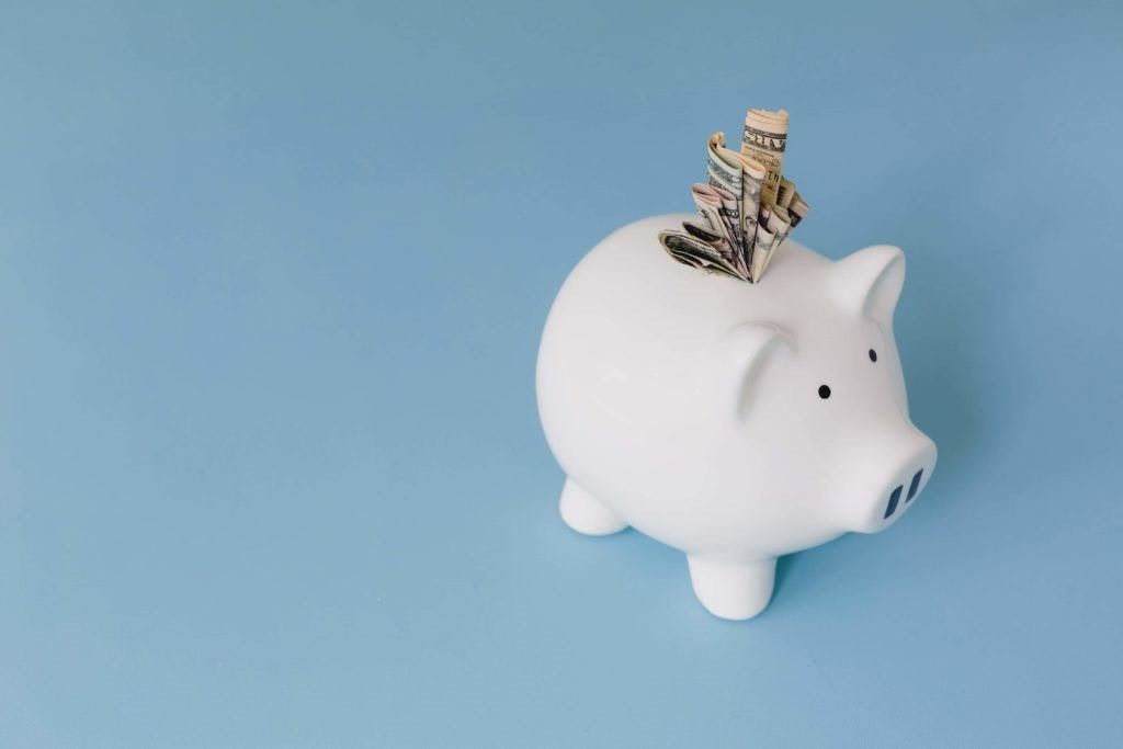 a blue background with a white piggy bank with bank notes jammed in the top