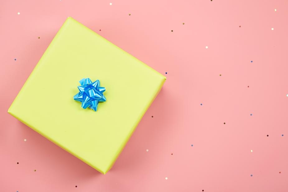An overheard shot of a gift wrapped in yellow paper with a blue bow