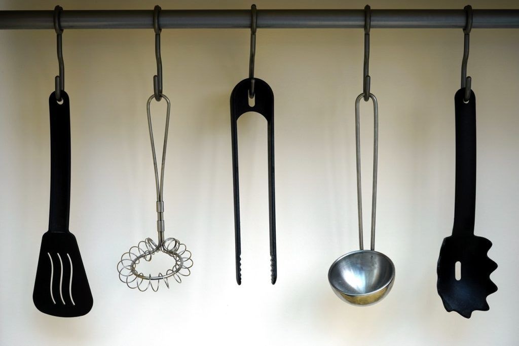 five kitchen utensils hanging from hooks