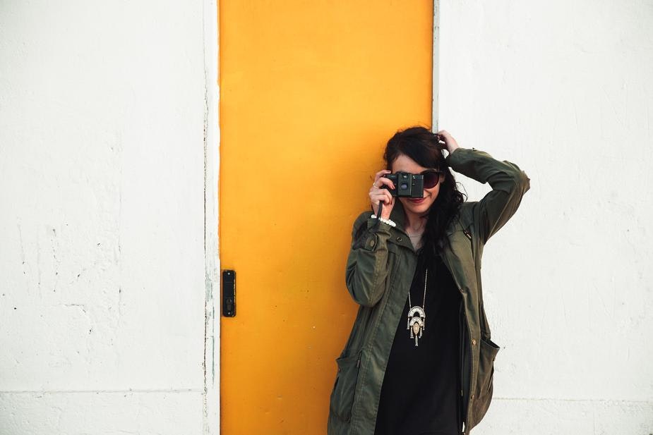 Woman stands against a yellow door taking a photo