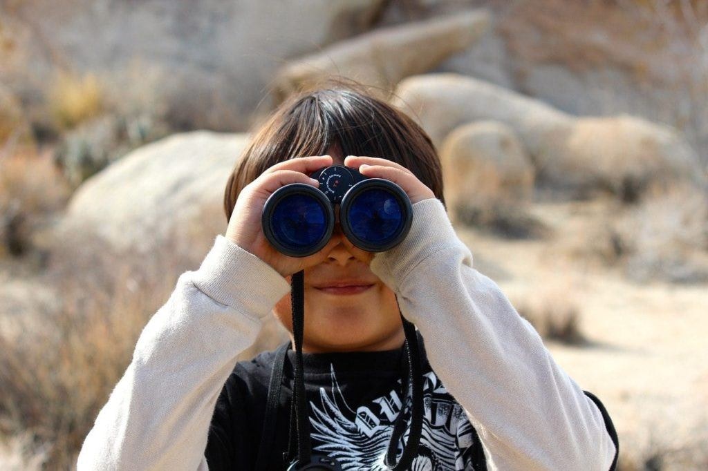 child peering through binoculars