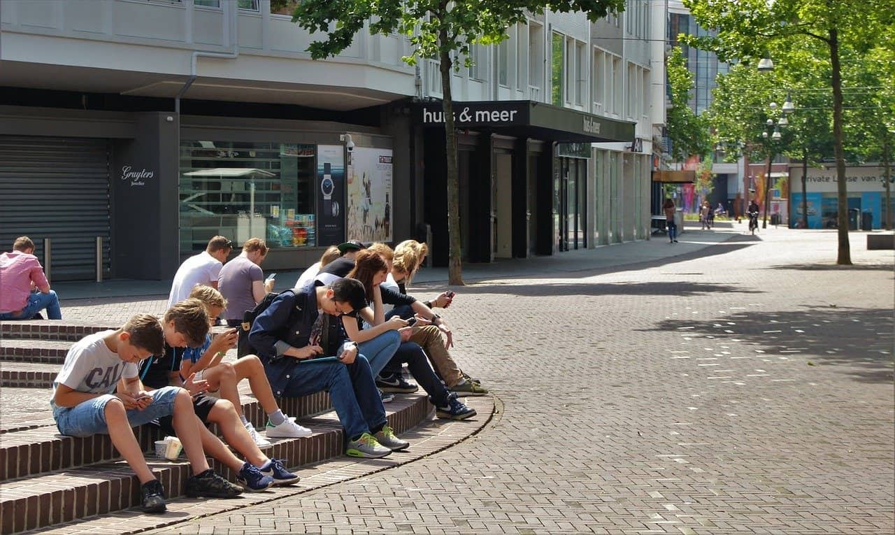 a bunch of teenagers sit on a street all looking at their phones