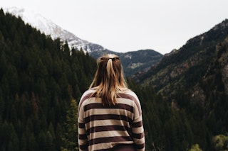 Woman in a striped jumper faces toward mountains