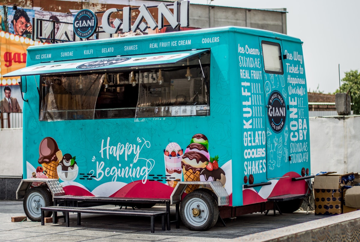 Ein hellblauer Food Truck mit Eis-Grafiken steht auf einem Parkplatz. Mit einem eigenen Food Truck gelingt dir ein niedrigschwelliger Einstieg in die Gastro-Szene und in die Selbstständigkeit.